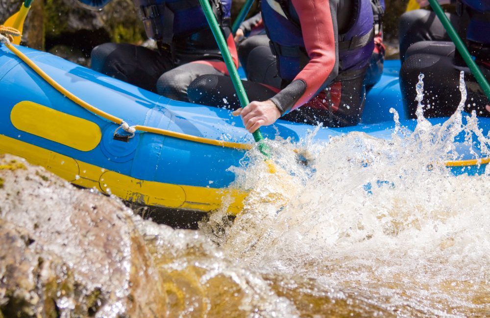 The shoulders down of individuals on a raft white water rafting and water splashing up the tube