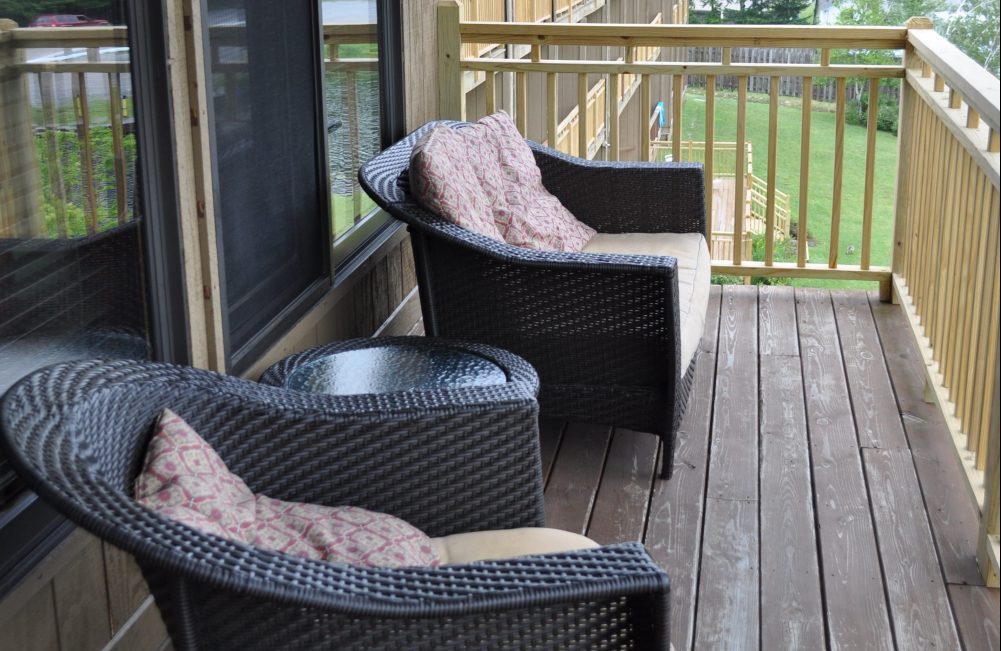 Two wicker chairs with cushions on a porch facing the lake