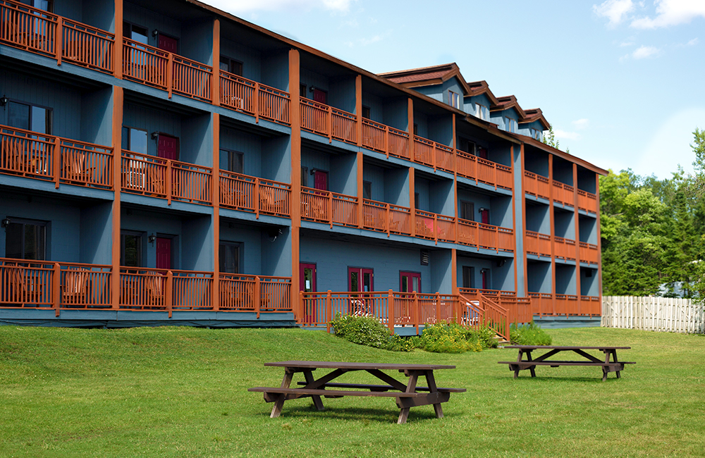Waters edge inn from the outside, its a wooden building with blue painted walls on the porches and Adirondack chairs outside of every room and two picnic tables outside