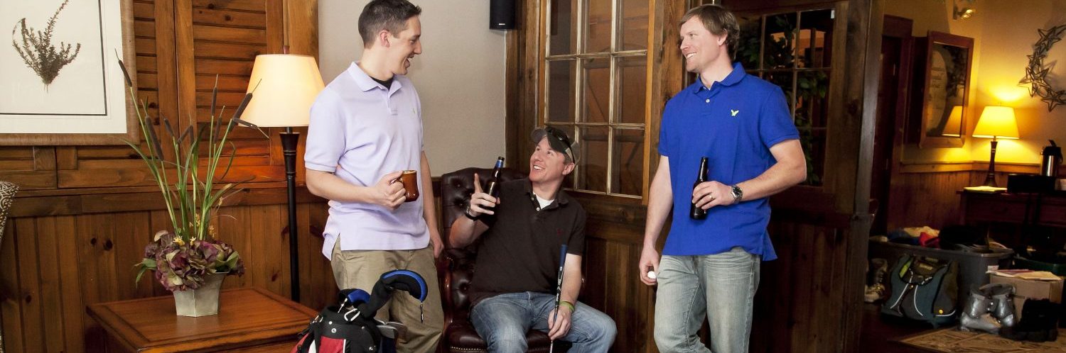 two guys standing with one guy sitting in the middle smiling in the middle of a conversation