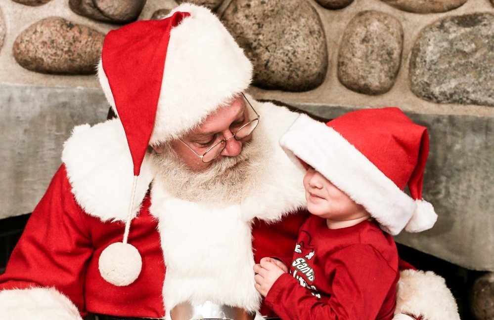 A young boy in a Santa hat sitting on Santas lap