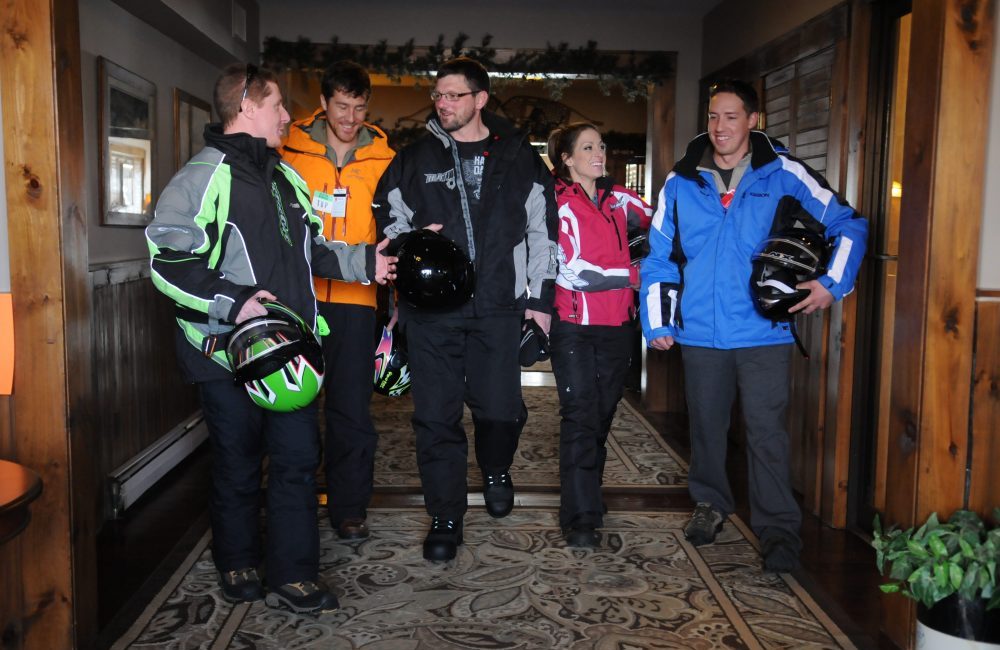 Five people in their winter gear holding snowmobiling helmets talking inside