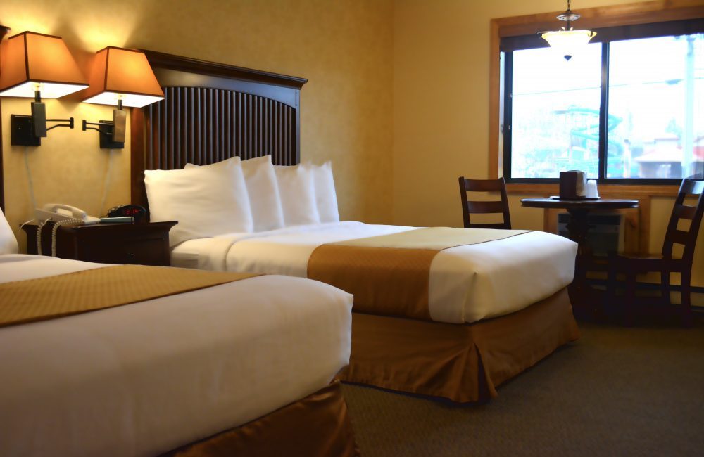 A hotel room with two beds with a nightstand between them and a small table with two chairs set up beneath a window