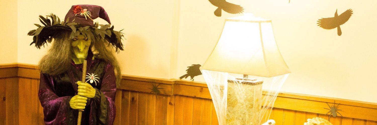 A table and lamp covered in fake spiderwebs and a fake witch and her cauldron beside the table