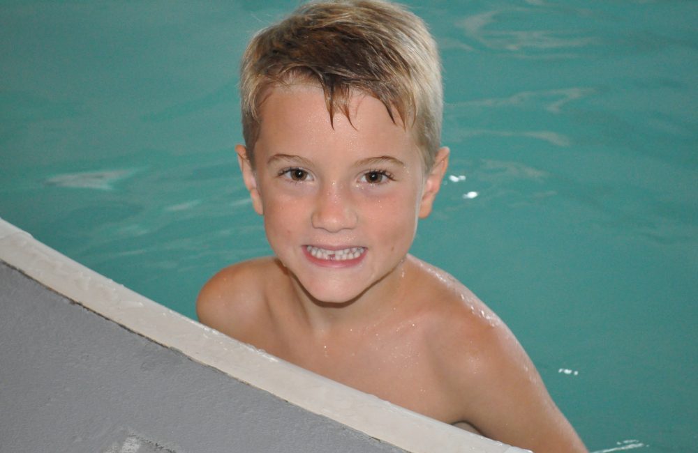 A boy in the pool on the edge smiling