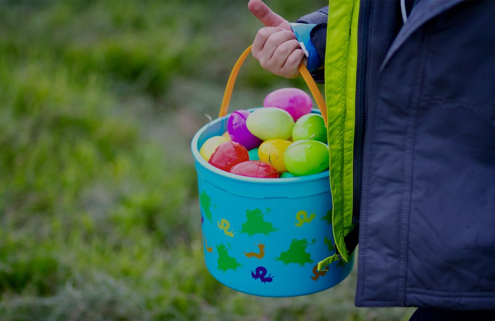 A kids hand holding a blue easter basket full of colorful plastic eggs