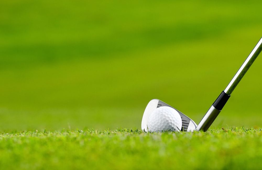 A gold ball and a golf club lined up behind it on the green