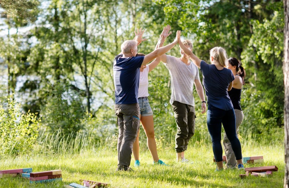 Full length of male and female coworkers giving high-five after playing with building blocks on field in forest