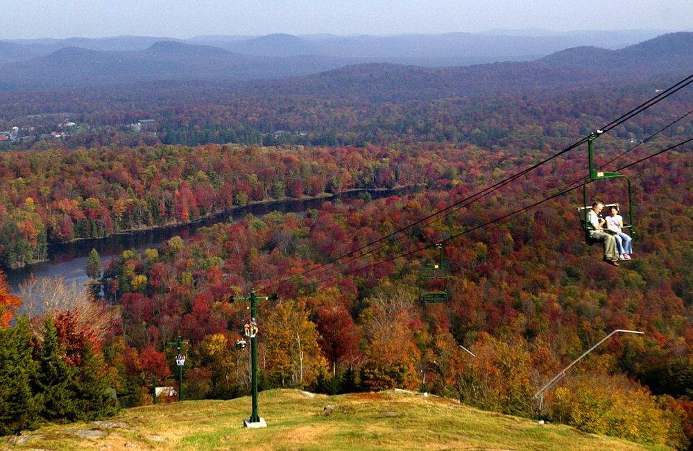 A father and daughter on a chairlift in the fall with the Adirondack mountains and a lake behind them