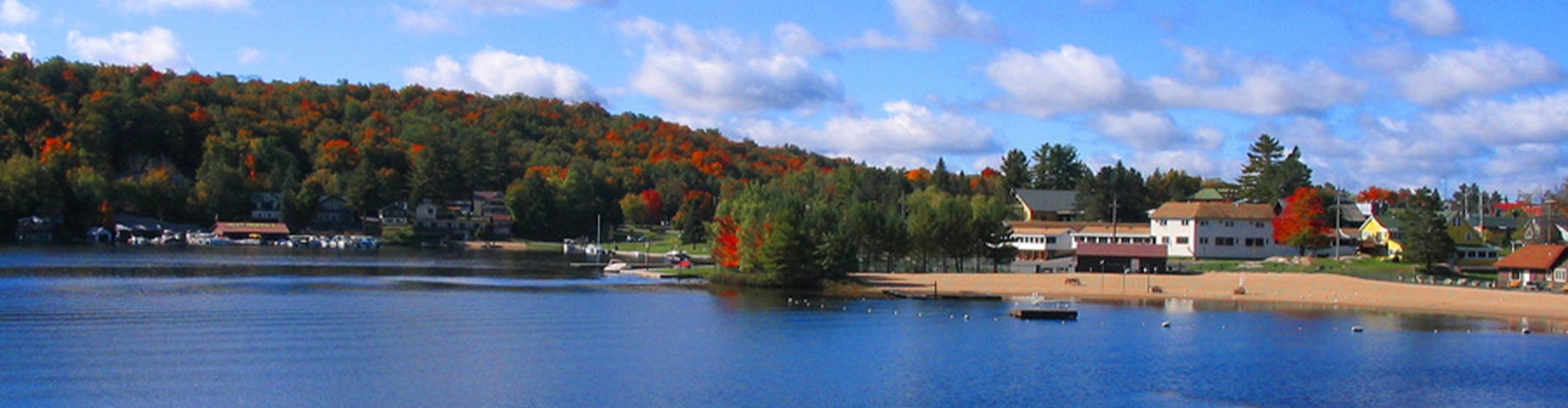 View from the docks of the blue lake and the tree line half green from pine trees and half red with fall foliage