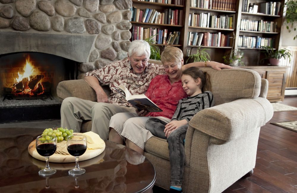 An older couple reading to their granddaughter by a roaring fire