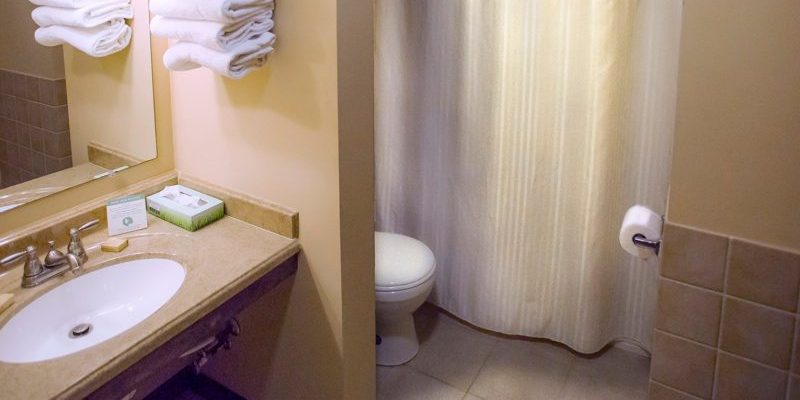 A bathroom with a white toilet, a bathtub with a shower curtain, a sink, and towels neatly stacked on a shelf next to the sink