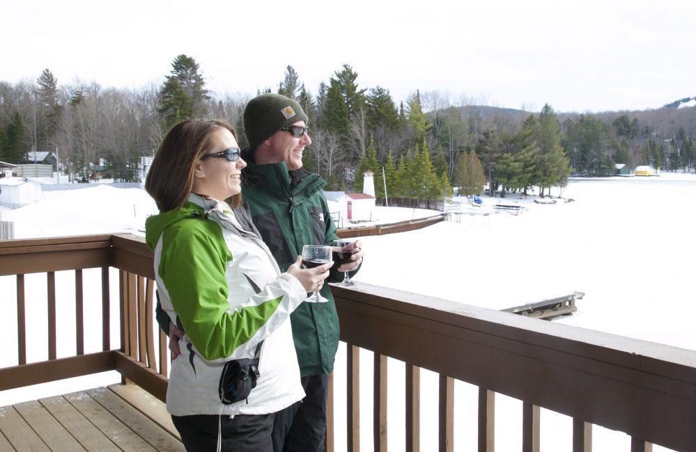 A couple in winter drinking wine on a porch looking at the frozen lake