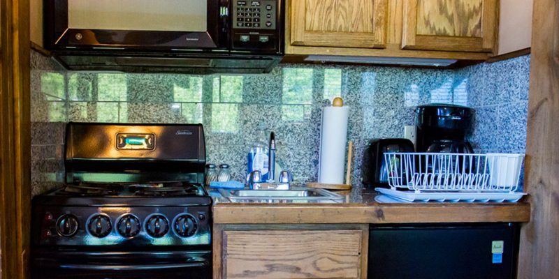 A kitchen with an oven/stove, a mini fridge, a microwave, a coffee maker, a sink, a dish rack, and wooden cabinets