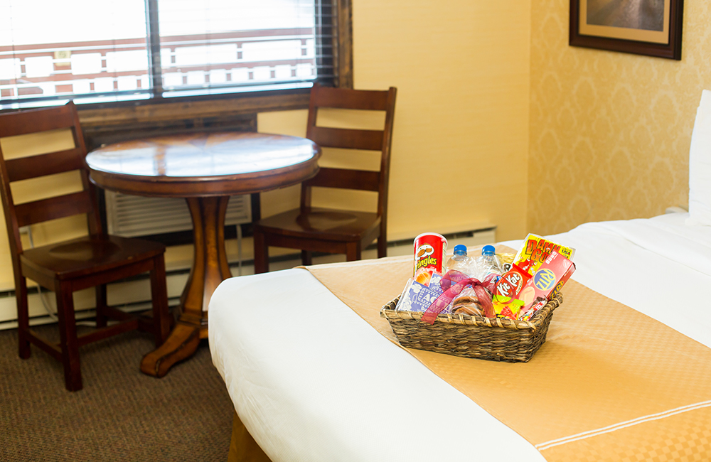 A hotel room bed with a movie night basket goodies on it