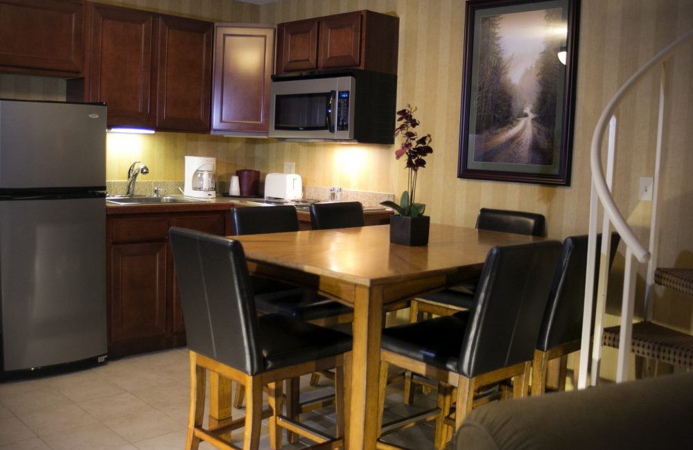 A kitchen with wooden cabinets, stainless steel appliances, a wooden table with flowers on it a wood and leather chairs around it