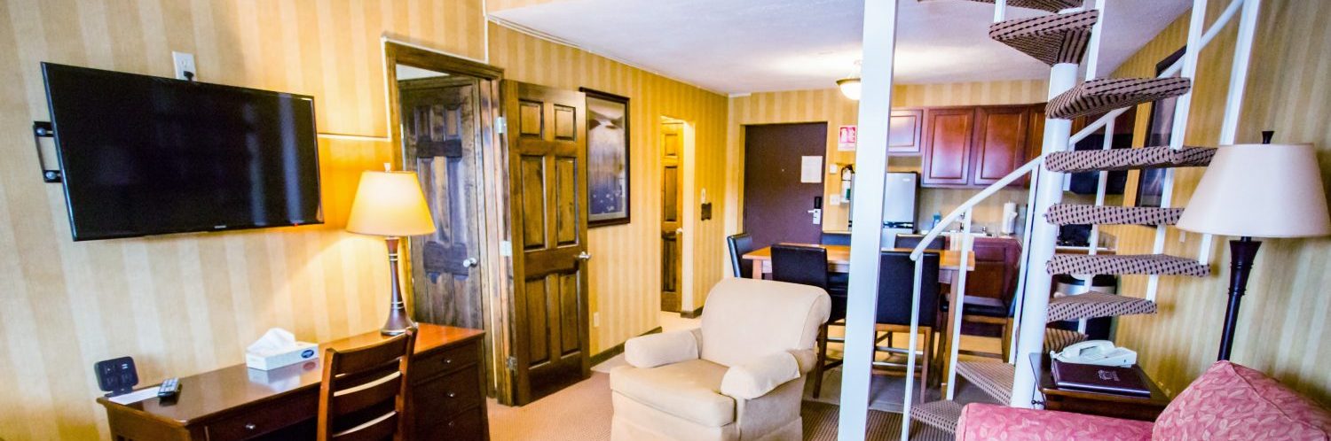 A living room that opens into a kitchen with a door to the left and a spiral staircase to the right