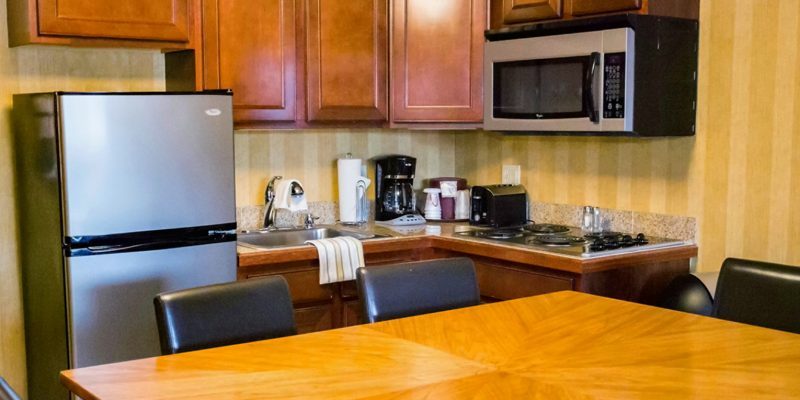 A kitchen with a fridge, sink, microwave, stove, coffee maker, toaster, wooden cabinets, and a wooden table