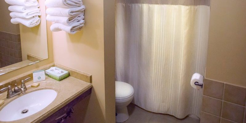 A bathroom with a white toilet, a bathtub with a shower curtain, a sink, and towels neatly stacked on a shelf next to the sink