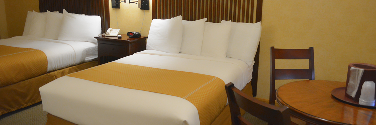A hotel room with two beds with a nightstand between them and a small table with two chairs