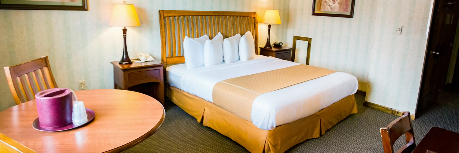 A hotel room with a king bed, two nightstands, and a small table and chairs