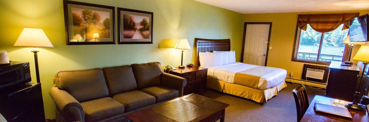 a hotel room with a fridge microwave couch bed desk dresser and tv mounted on the wall