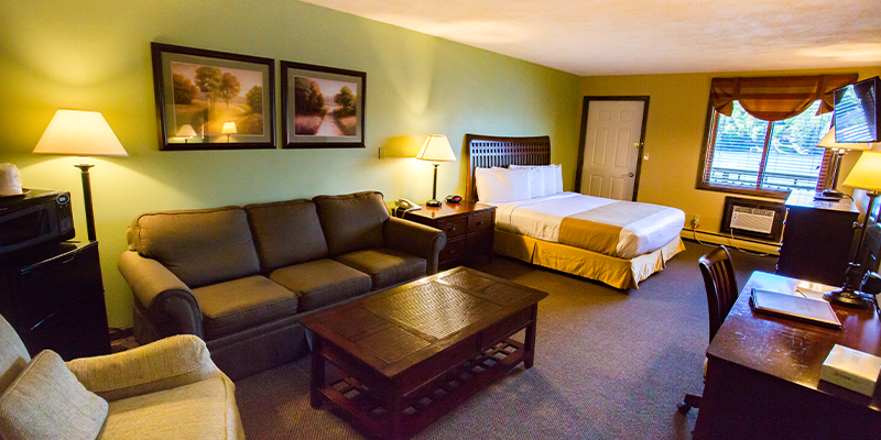 a hotel room with a fridge microwave couch bed desk dresser and tv mounted on the wall