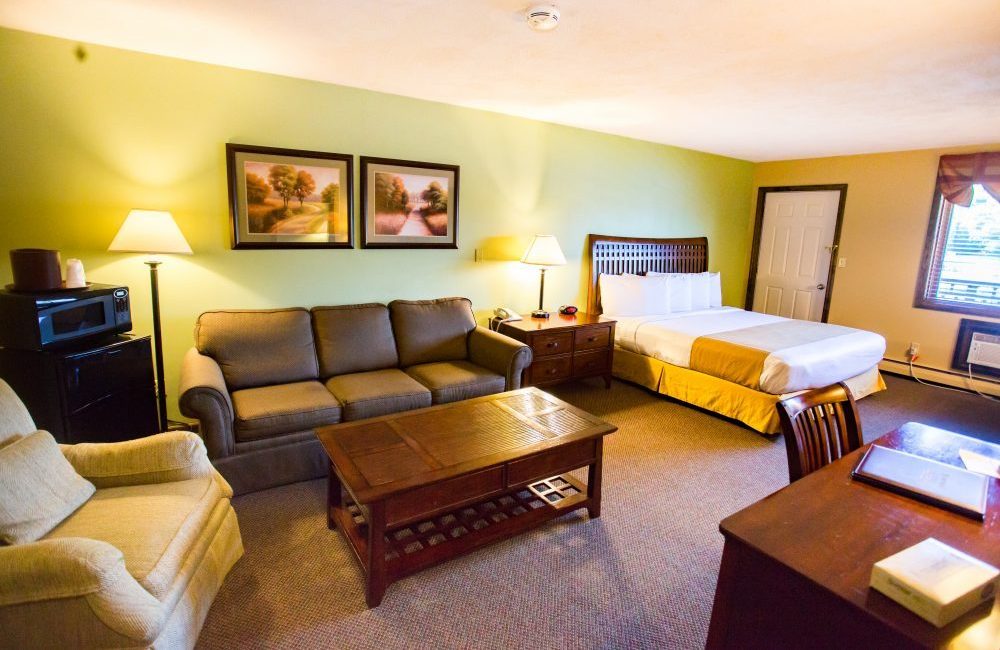a hotel room with a fridge microwave couch bed desk dresser coffee table and a chair