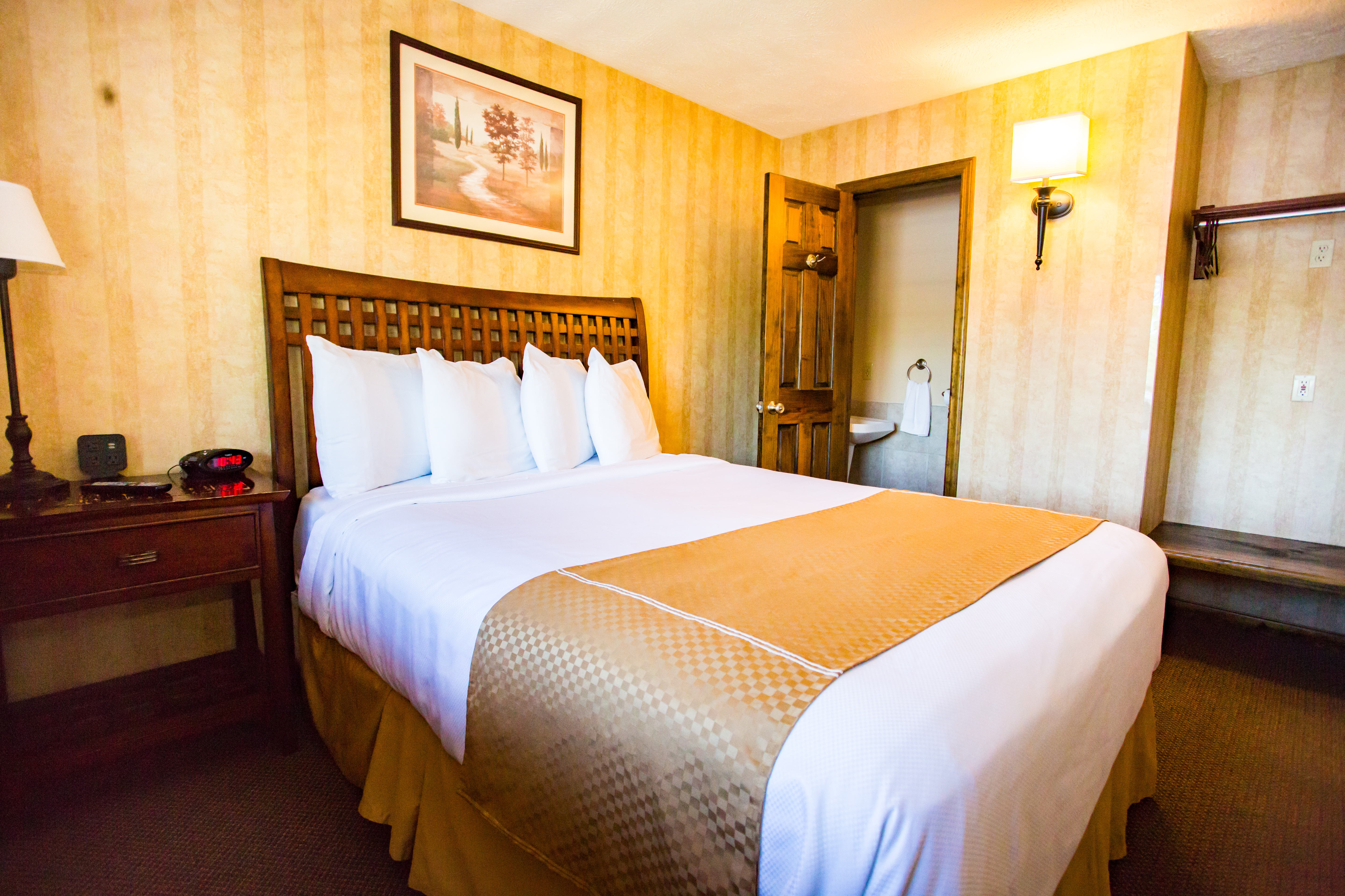 a night stand next to a bed next to a bathroom in a hotel room