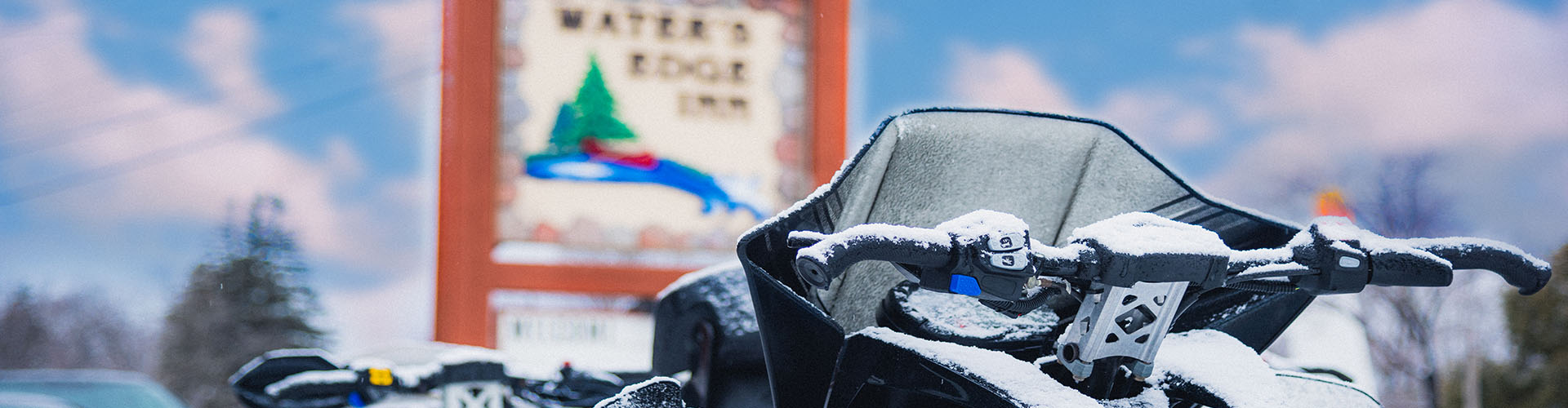 Snow covered snow mobile with blurred Water's Edge Inn sign in the background